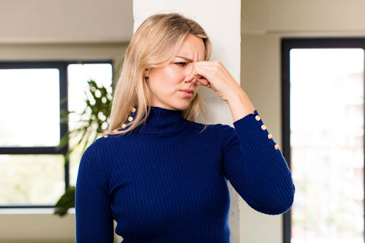 A Woman Standing In A Home And Holding Her Nose Because Of A Bad Smell.