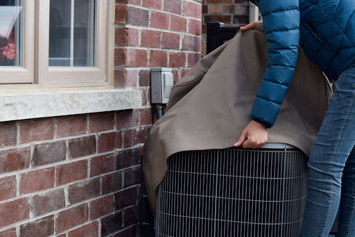 Someone putting a cover on an outdoor AC unit outside of a house.