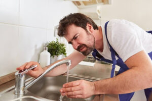 A man checking the water flowing out of a kitchen sink.