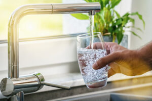 A hand filling a glass of water at a kitchen faucet.