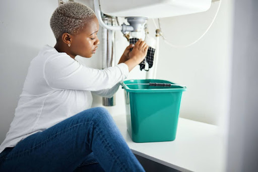 A woman holding a rag up to a leaking pipe under a sink.