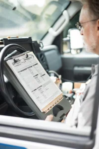 A person sits in a vehicle reviewing a clipboard with a printed checklist or inspection form, ensuring all tasks align with the maintenance plan.