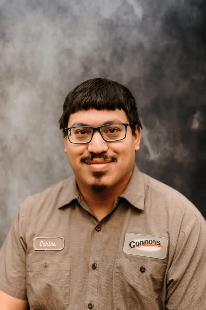 A Connors team member with short dark hair, glasses, and a mustache smiles in uniform before a marbled gray background.
