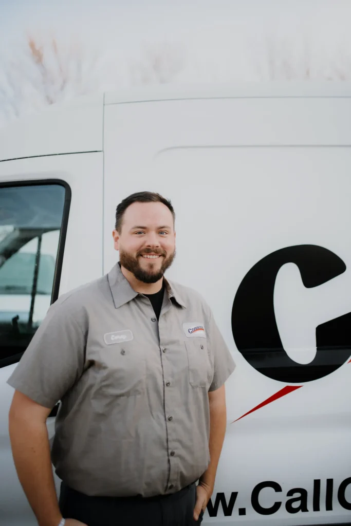 A friendly Connors team member in a gray work shirt smiles by a branded van, ready to help—meet our crew on the About Us page.