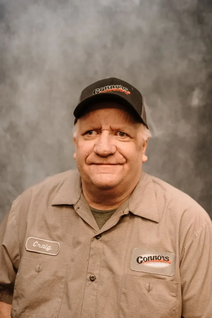 Craig, a friendly Connors team member in uniform, poses proudly for our About Us section against a neutral gray background.