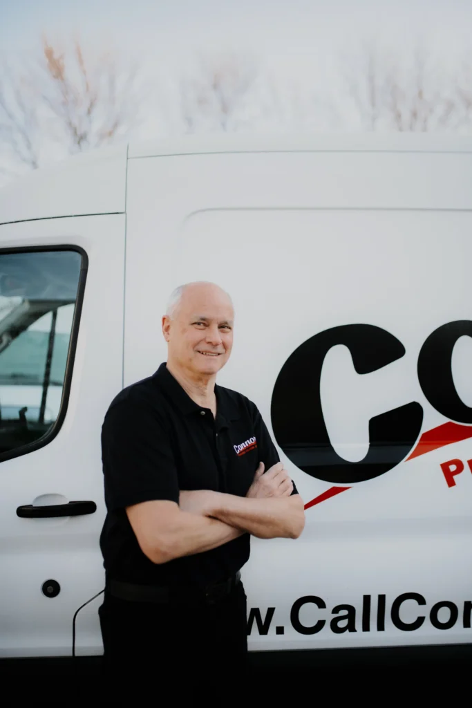 A Connors Plumbing, Heating, Air, & Electrical team member stands confidently by a branded service van, ready to help customers.
