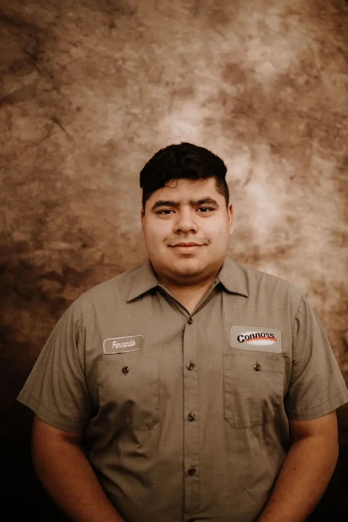 Fernando, a Connors technician in uniform, smiles warmly against a brown backdrop, showcasing our welcoming team members.