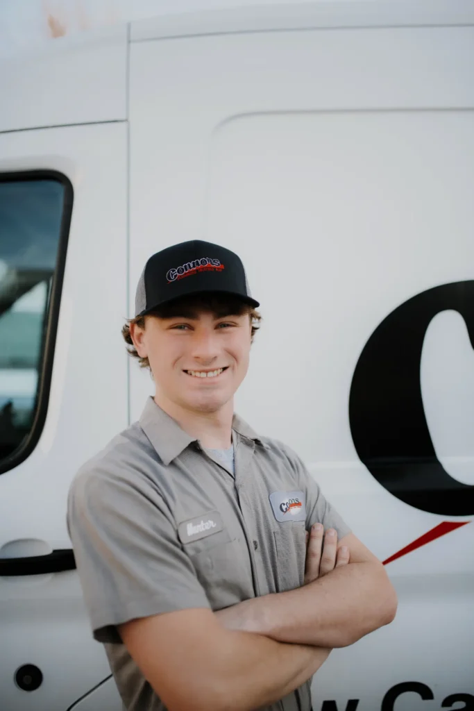 A friendly Connors team member in uniform stands confidently with arms crossed in front of a branded company van.