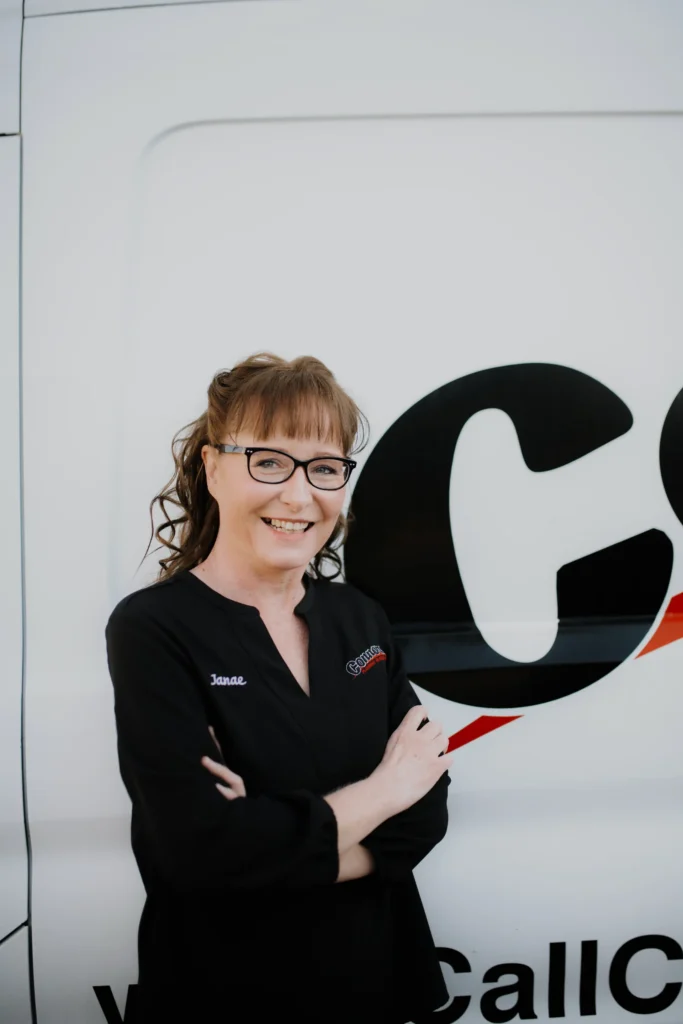 A friendly Connors team member with glasses and brown hair stands smiling, arms crossed, in front of a branded service van.