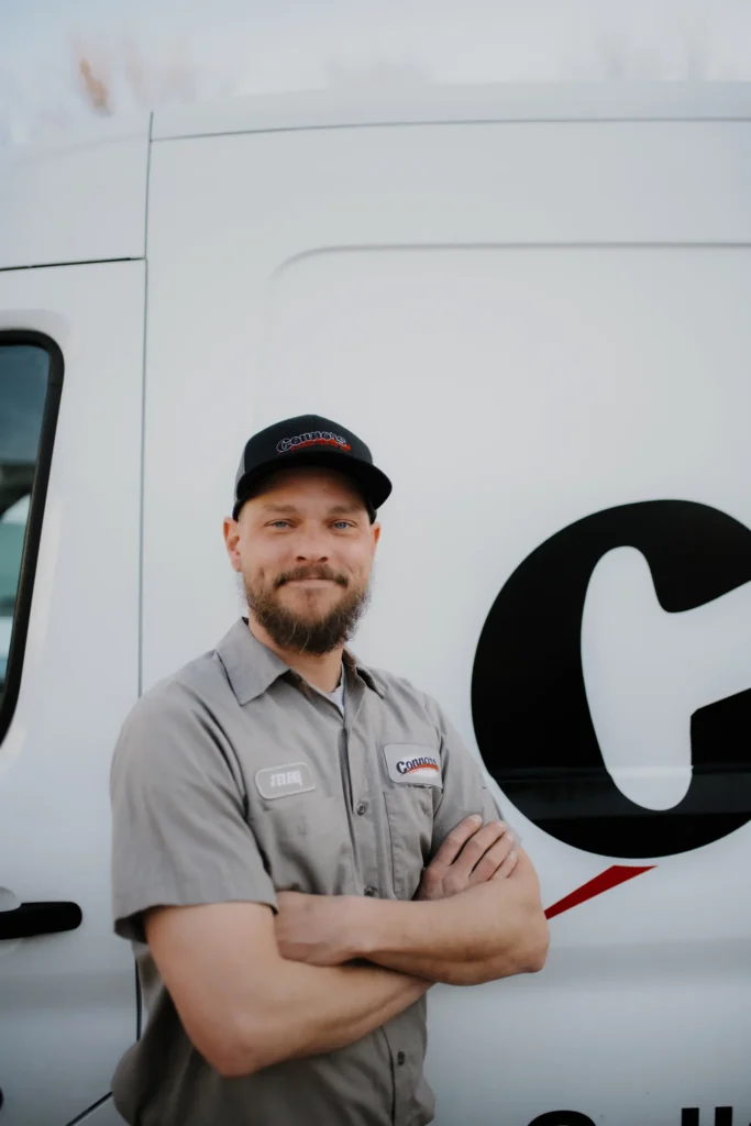A Connors team member in uniform stands confidently with arms crossed before a branded service van, ready to serve our community.