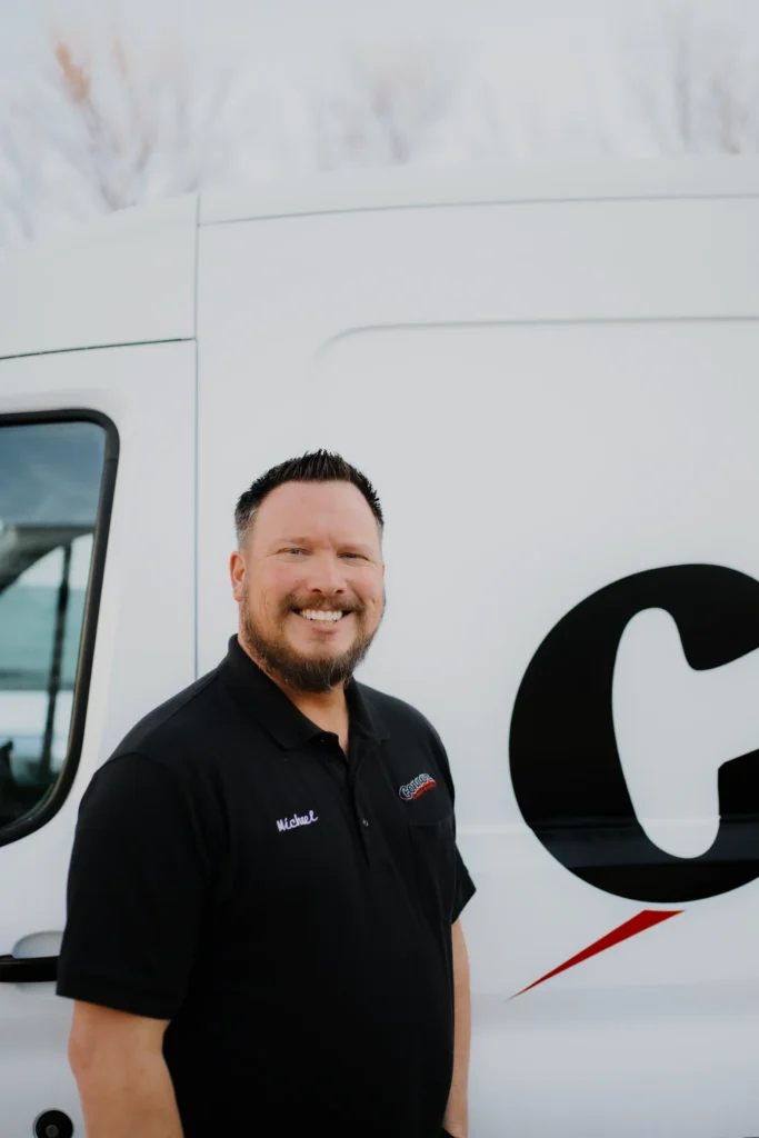A friendly, bearded Connors team member in a black polo stands by a branded service van, reflecting our company values.