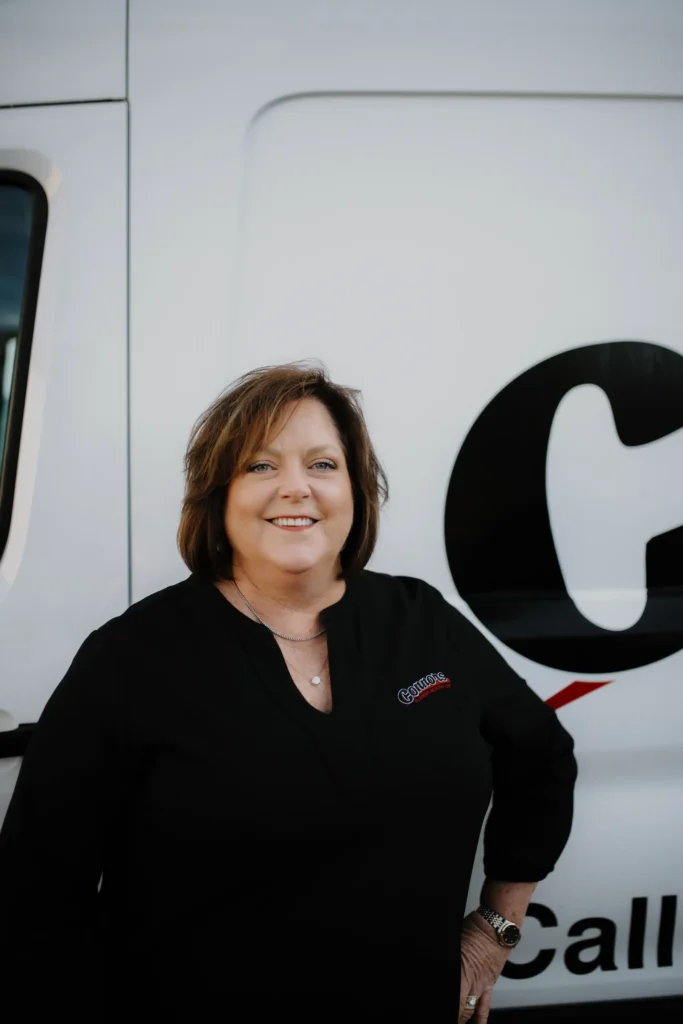 A friendly Connors Plumbing, Heating, Air, & Electrical team member smiles in front of a branded company vehicle.