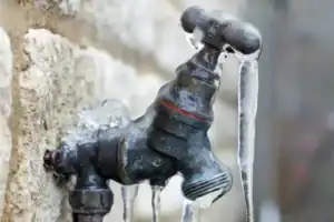 An outdoor faucet with icicles on a stone wall, showing freezing temps—a reminder from Connors to protect your pipes this winter.