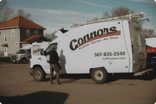 A person stands next to a white Connors service van parked outside, with company contact details and services listed on the side of the vehicle.